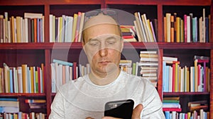 Adult caucasian white man use smart phone at bookshelf background home library