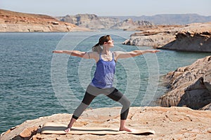 Adult woman doing yoga lakeside in warrior 2 pose photo