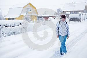 Adult Caucasian woman portrait standing with on snowy road in village during strong snowfall, hiker with backpack