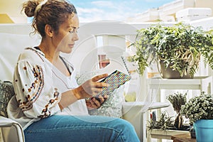 Adult caucasian woman reading a book outside home inthe terrace in relax leisure activity. One female people studying from paper