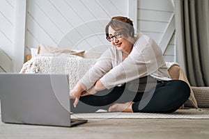 Adult charming brunette woman plus size body positive practice yoga with laptop at home