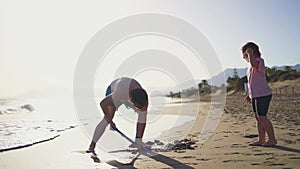 An adult and child engage in digging sand at a sunlit beach, representing a family vacation moment with gentle ocean