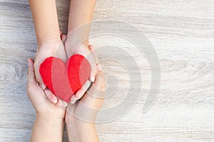 Adult and child hands holding handmade red heart on wooden background.