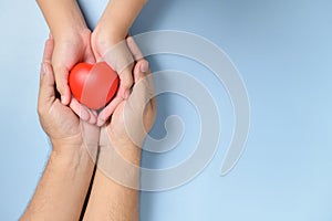 Adult and child hands holding red heart  on blue background