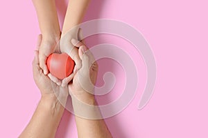 Adult and child hands holding red heart  on pink