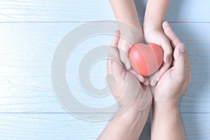 Adult and child hands holding red heart on vintage