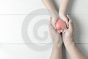 Adult and child hands holding red heart on vintage tone