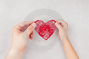 Adult and child holding red heart in hands from above. Family relationships, health care, pediatric cardiology concept.