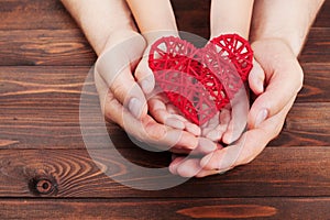 Adult and child holding red heart in hands over a wooden table. Family relationships, health care, pediatric cardiology concept. photo