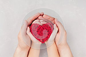 Adult and child holding red heart in hands top view. Family relationships, health care, pediatric cardiology concept. photo