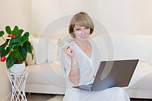 Adult confident pretty woman working with laptop and credit card at home in stylish living room