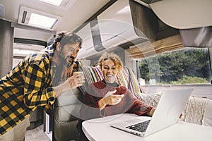 Adult couple enjoy work together using laptop computer sitting inside camper rv vehicle. Concept of nomad and alternative free job