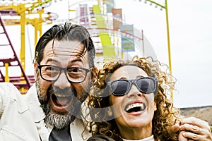 An adult couple of man and woman show expressions and fun during an extreme roller coaster ride. Smiling people have fun at