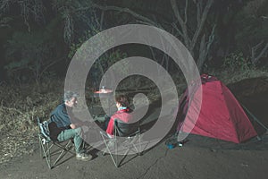 Adult couple relaxing in camping site by night. Adventure in National Park, South Africa. Burning camp fire and tent in the backgr