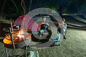 Adult couple relaxing in camping site by night. Adventure in National Park, South Africa. Burning camp fire and tent in the backgr