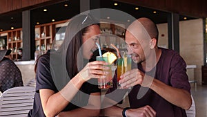 An adult couple is sitting in the hotel bar and clinking bright cocktails.