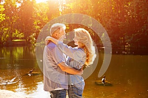 An adult couple stand on the shore of the lake in an embrace in the rays of the setting sun