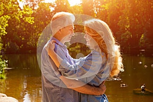 An adult couple stand on the shore of the lake in an embrace in the rays of the setting sun