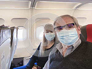 Adult couple taking a selfie while travelling by plane wearing a surgical mask during the covid pandemic