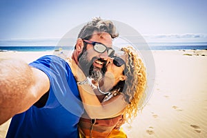 Adult couple of tourist take selfie picture at the beach with sand and blue ocean and sky in background. Hapy man and woman