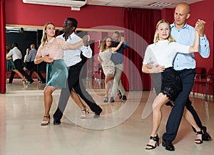 Adult couples dancing salsa dance together in modern studio