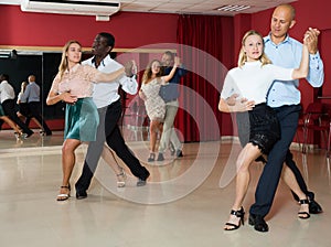 Adult couples dancing salsa dance together in modern studio