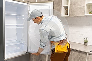 adult craftsman in working overall writing in clipboard near broken refrigerator in kitchen