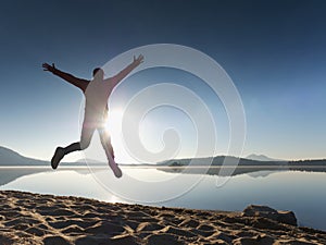 Adult crazy man jumps near water on against red sunset. Empty beach