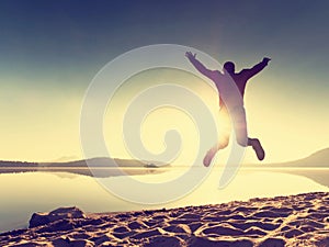 Adult crazy man jumps near water on against red sunset. Empty beach