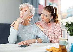 Adult daughter calming upset mother after quarrel at table