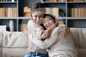 Adult daughter cuddling cherish her mother women seated on couch