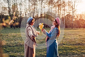 Adult daughter giving flowers as present to her senior mother in spring park. Mother`s day concept. Family values