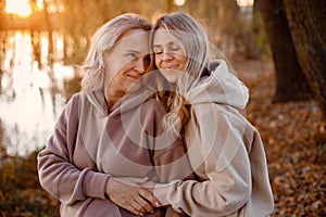 Adult daughter hugs her pregnant mom while standing in autumn park