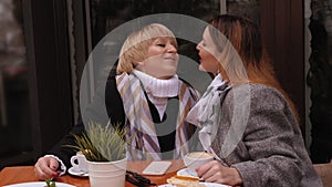 An adult daughter kisses her elderly mother when they meet in a street cafe.