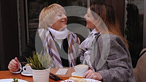 An adult daughter kisses her elderly mother in a street cafe in the spring.