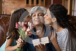 Adult daughter little granddaughter greeting mature latin lady with birthday