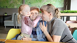Adult daughter and little granddaughter kiss their grandmother.