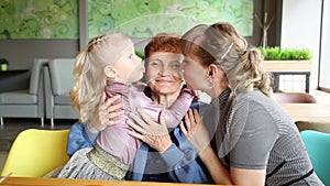 Adult daughter and little granddaughter kiss their grandmother.