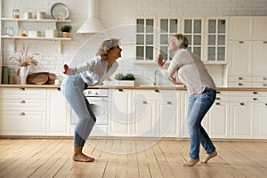 Adult daughter and mother dancing at modern kitchen celebrate renovation