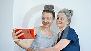 Adult daughter and senior mum are taking self-portrait picture, selfie on red smartphone together, happy retirement