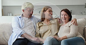 Adult daughter sits on sofa with old mother and father