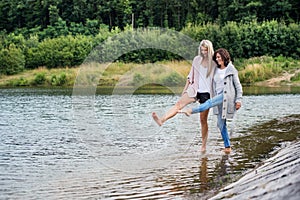 Adult daughter spending time with her mother. Mom and daughter outdoors, walking barefoot in water of lake reservoir