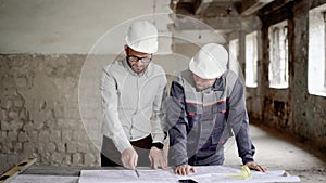 An adult engineer explains to the worker a new construction plan, which was designed by the architect, people are in an