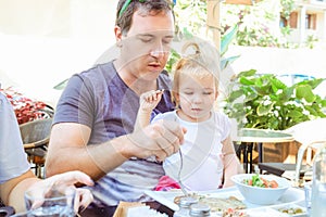 Adult Father feeding his cute toddler daughter during family breakfast in outside cafe. Family rest, spending time together concep