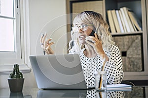 Adult female entrepreneur at work busy in phone call and explaining solutions to colleagues in remote office workplace. Online job