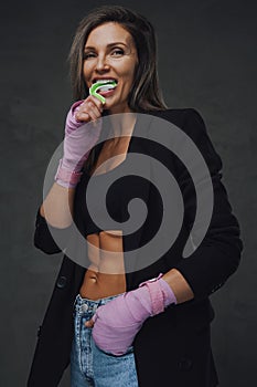 Adult female fighter with bandaged arms bites mouth guard in studio
