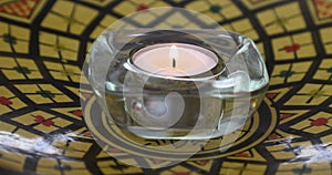 Adult female hands lighting a tea light with a match in a glass candle holder on a yellow plate