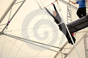 An adult female hangs on a flying trapeze at an indoor gym. The woman is an amateur trapeze artist