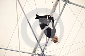 An adult female hangs on a flying trapeze at an indoor gym. The woman is an amateur trapeze artist