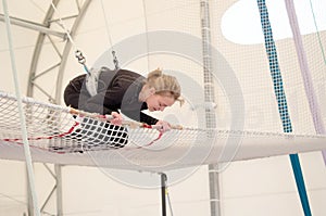 An adult female lands on a net, preparing to dismount at a on a flying trapeze school at an indoor gym. The woman is an amateur